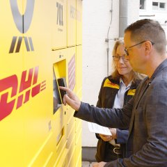 Bürgermeister Holger Siemon trägt gemeinsam mit Gabriele Schulz (regionale Politikbeauftragte der DHL Group) die Daten für die erste Paketaufgabe am Touchscreen der neuen Poststation ein