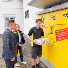 Jonas Sauerwald (Mitarbeiter der Deutschen Post) zeigt Gabriele Schulz (regionale Politikbeauftragte der DHL Group) und Bürgermeister Holger Siemon die Abholung der Pakete und Briefe aus der Poststation